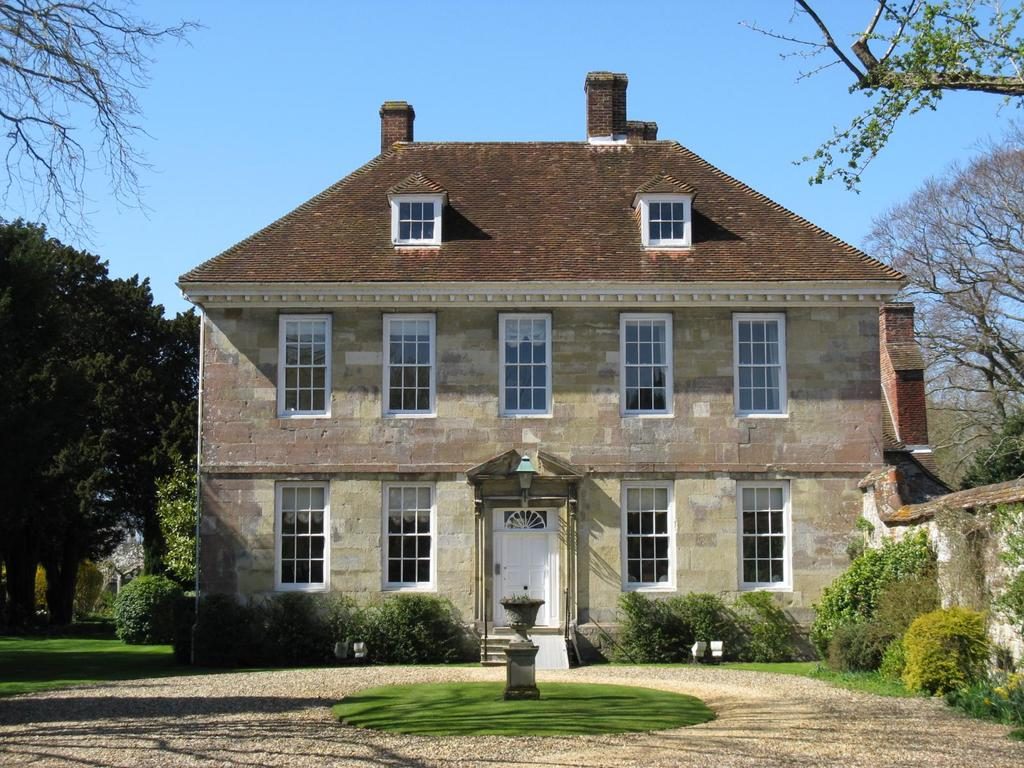A stone Georgian-style house with tall sash windows, a gravel drive and a round lawn