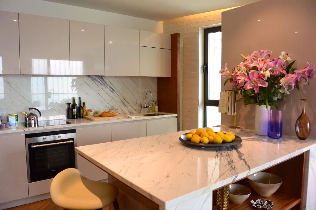 A modern kitchen with glossy white cabinets, a marble island, a bowl of lemons and fresh lilies