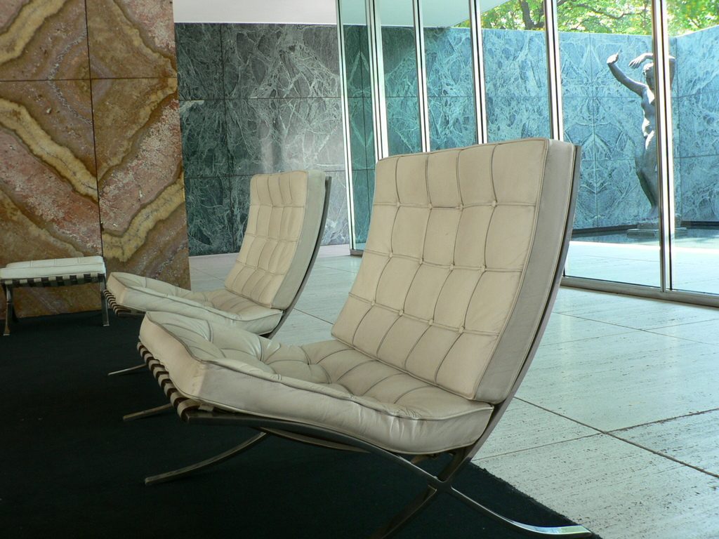 Two cream leather lounge chairs in a bright room with marble walls and floor-to-ceiling glass