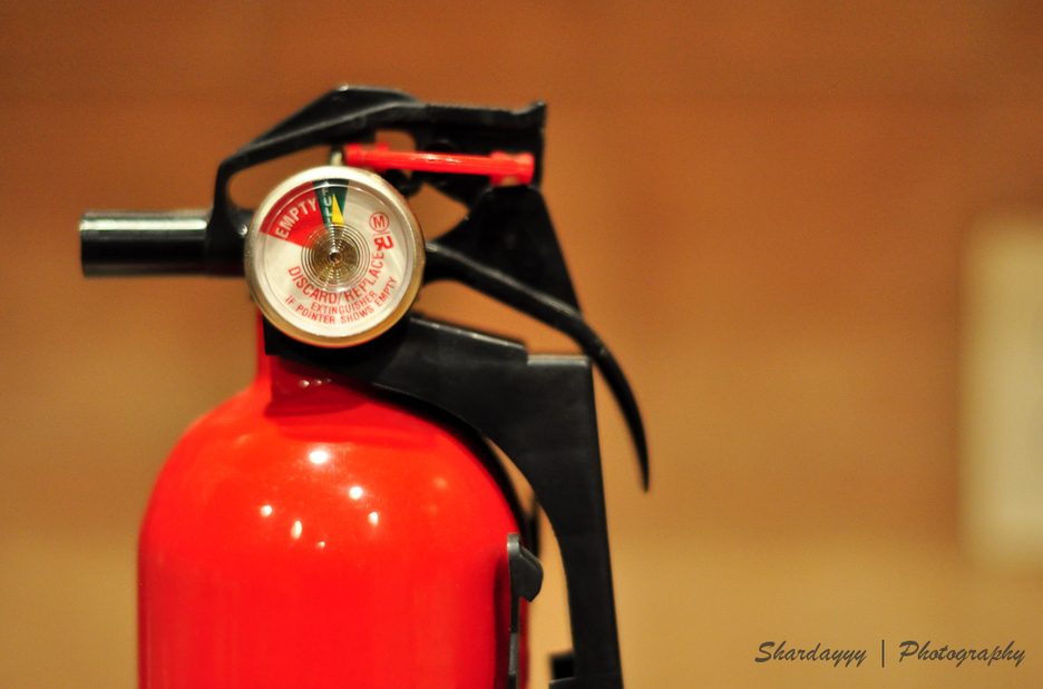 Close-up of a red fire extinguisher with its pressure gauge and black handle