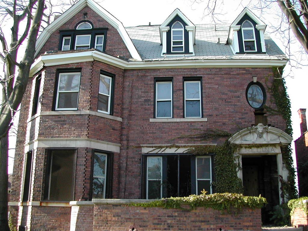 A tall red brick house with white dormer windows and ivy around the front door