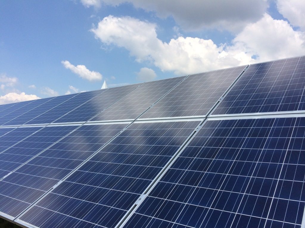 Rows of blue solar panels angled toward a bright sky with white clouds